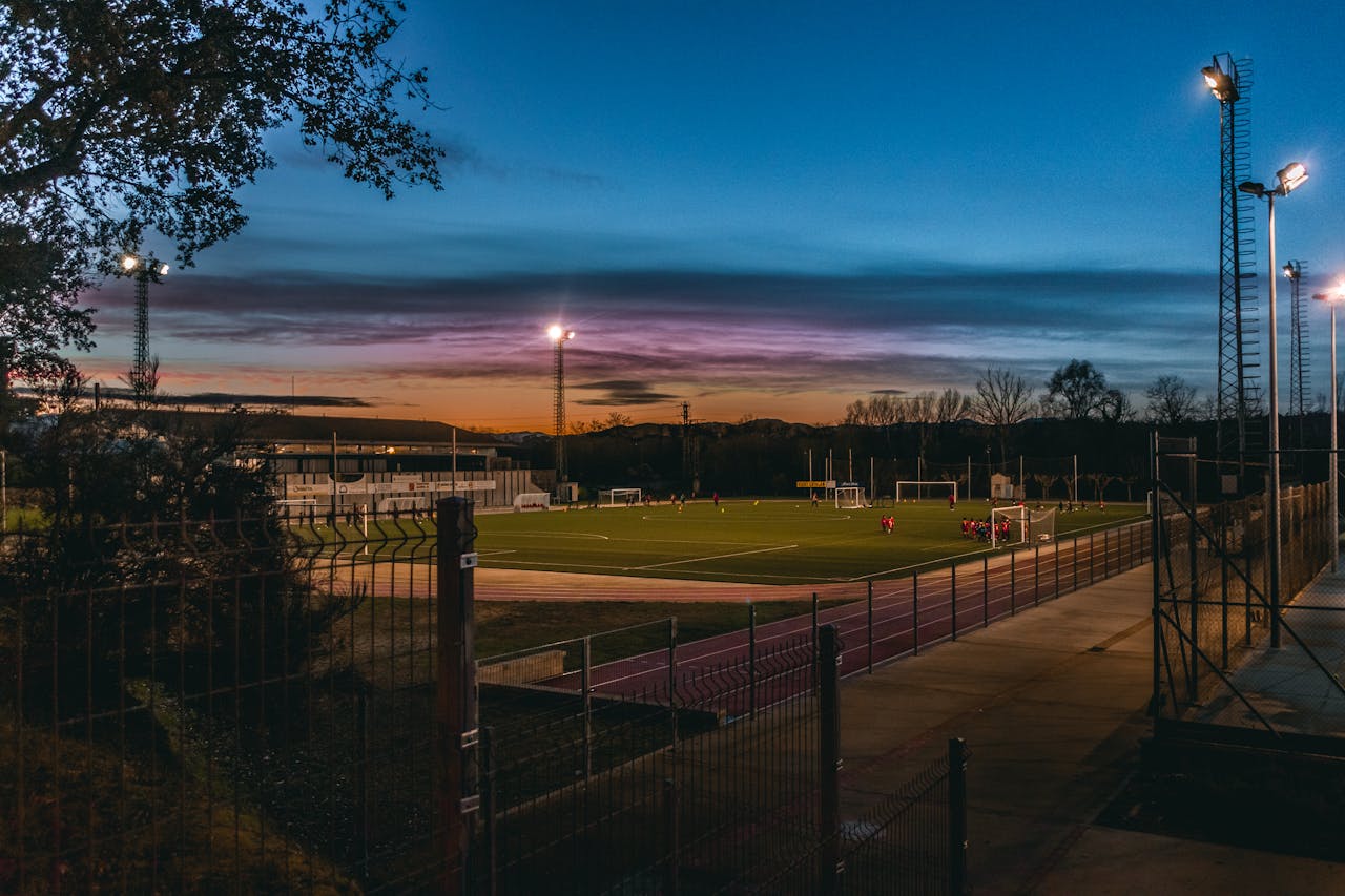 Football field illuminated by stadium lights at dusk with players practicing.